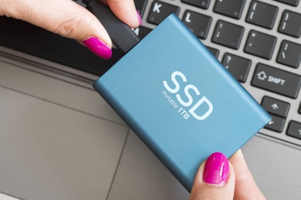 Portable SSD state solid drives disk in woman’s hands against notebook keyboard